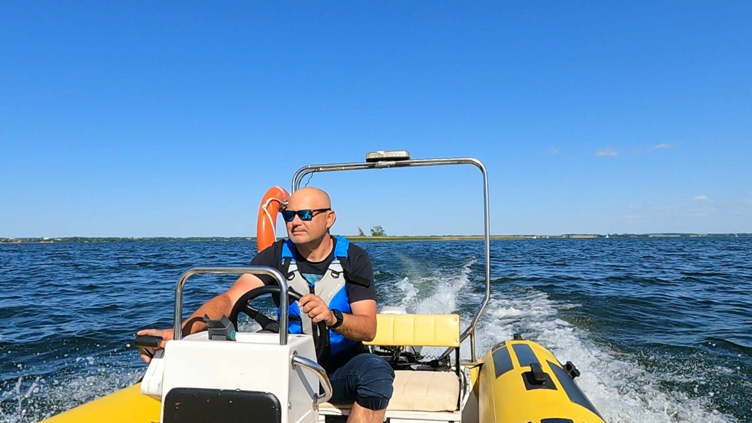 Przystojny instruktor na szkoleniu na stopień sternika motorowodnego, płynący jachtem motorowym typu RIB w piękną pogodę na jeziorze Niegocin.