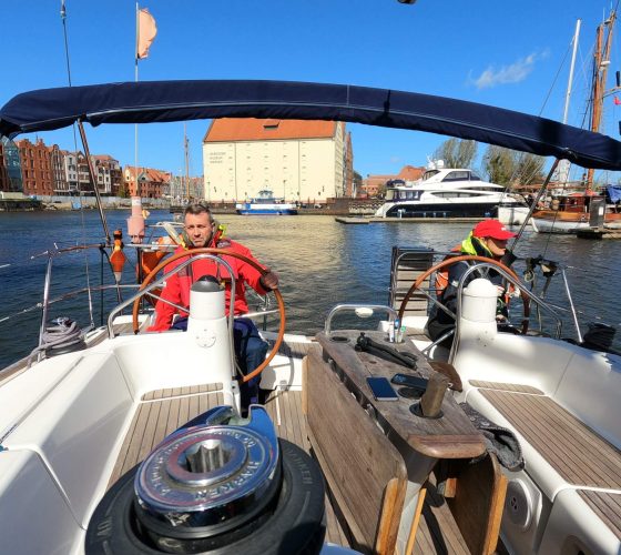 Instruktor za kołem sterowym morskiego jachtu podczas kursu z manewrowania jachtem żaglowym w porcie na Motławie w Gdańsku